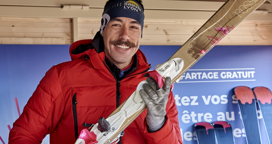 Animateur en gilet rouge portant des skis à la main