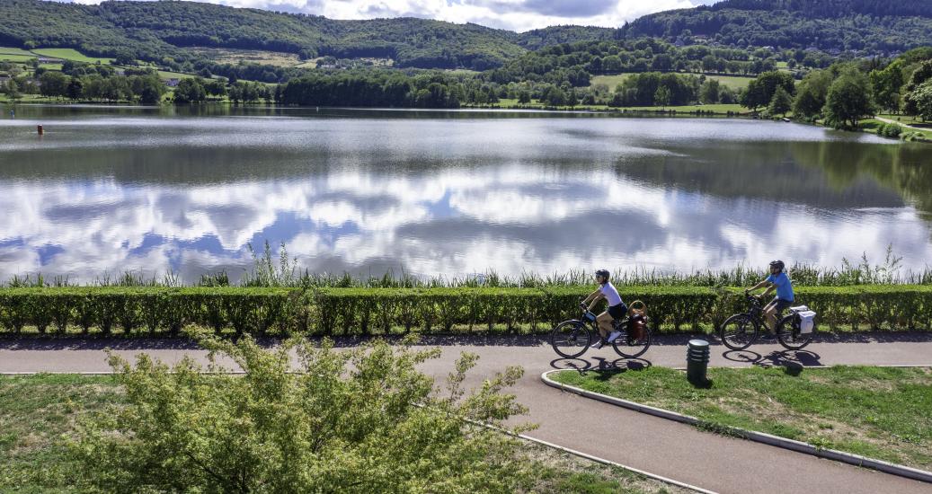 Deux vélos sur une voie bleue de la Cycloroute71 avec un paysage autunois en fond et un lac