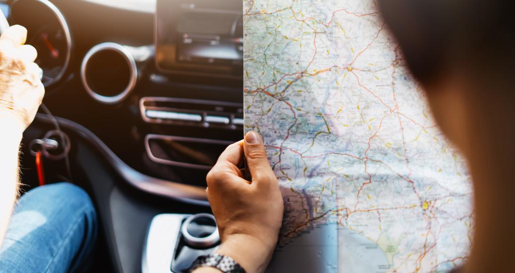 Hipster man holding in male hands and looking on navigation map in auto, tourist traveler hiker driving on background view way road, trip in transportation, person sitting on backdrop window auto