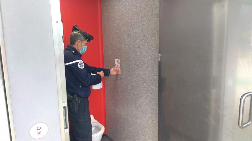 Un colonel de gendarmerie colle un sticker dans les sanitaires d'une aire d'Autoroute