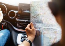 Hipster man holding in male hands and looking on navigation map in auto, tourist traveler hiker driving on background view way road, trip in transportation, person sitting on backdrop window auto